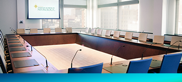 An empty meeting room with chairs in a rectangle formation and a screen with AAN's logo