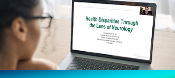 A woman in glasses looks at a screen that says 'Health Disparities Through the Lens of Neurology'